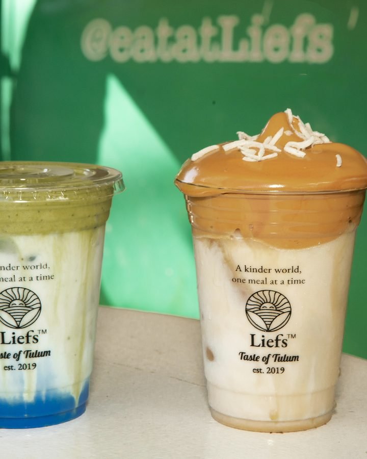 Matcha latte and cafe espuma coffee with coconut flakes in front of the green @eatatLiefs sign at Liefs Tulum